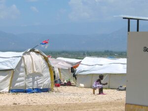 An image of a child sitting outside a tent encampment in Haiti.